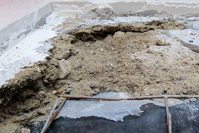 A layer of bedding mortar, partly broken out, exposing Incorrectly positioned mesh and damp-proof-membrane.